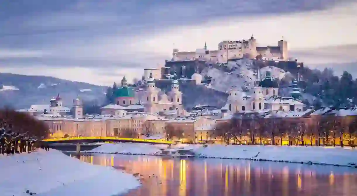 Salzburg with famous Festung Hohensalzburg and Salzach river illuminated in beautiful twilight during scenic Christmas time