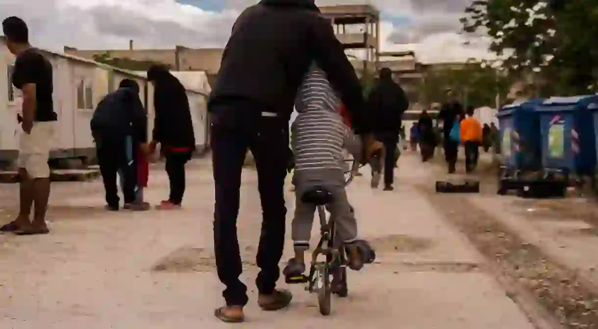 A father teaches his son how to cycle on a flat-tire bike in Eleonas Refugee Camp