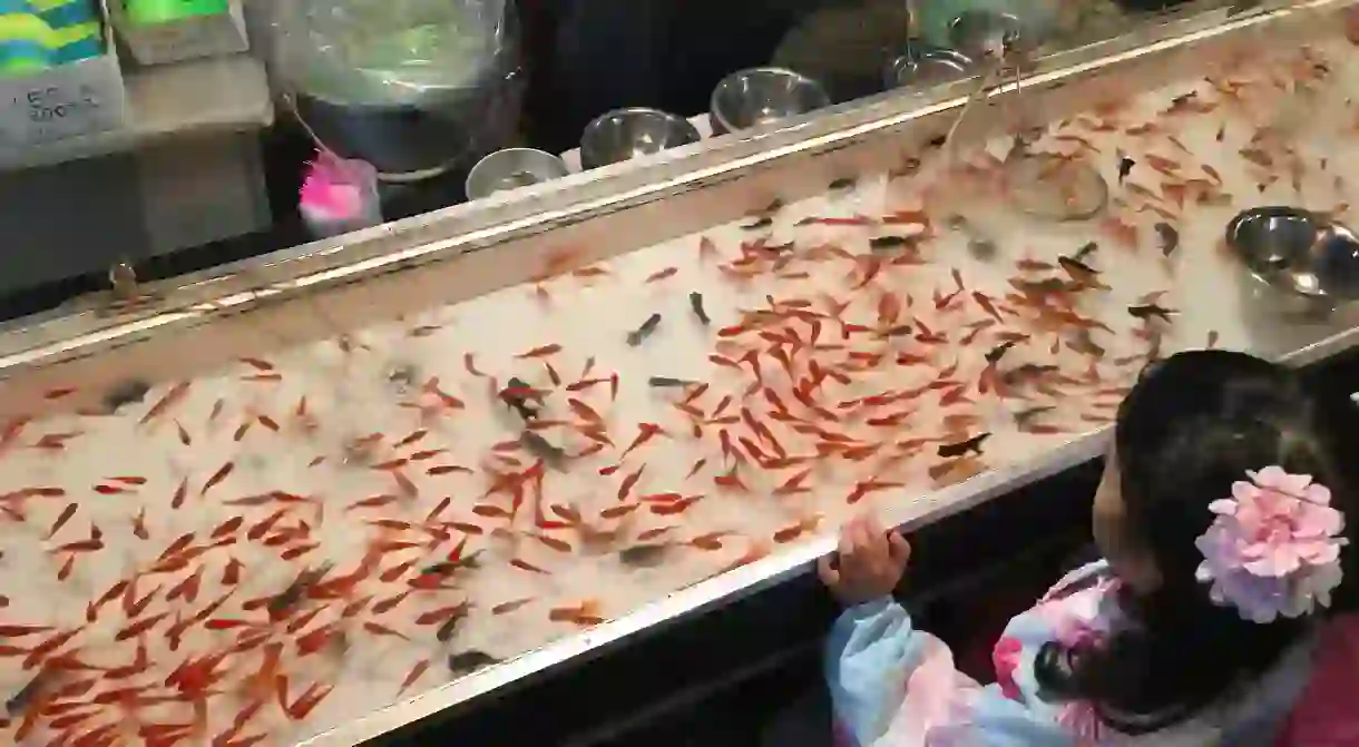 A little girl in yukata prepares for a round of goldfish scooping