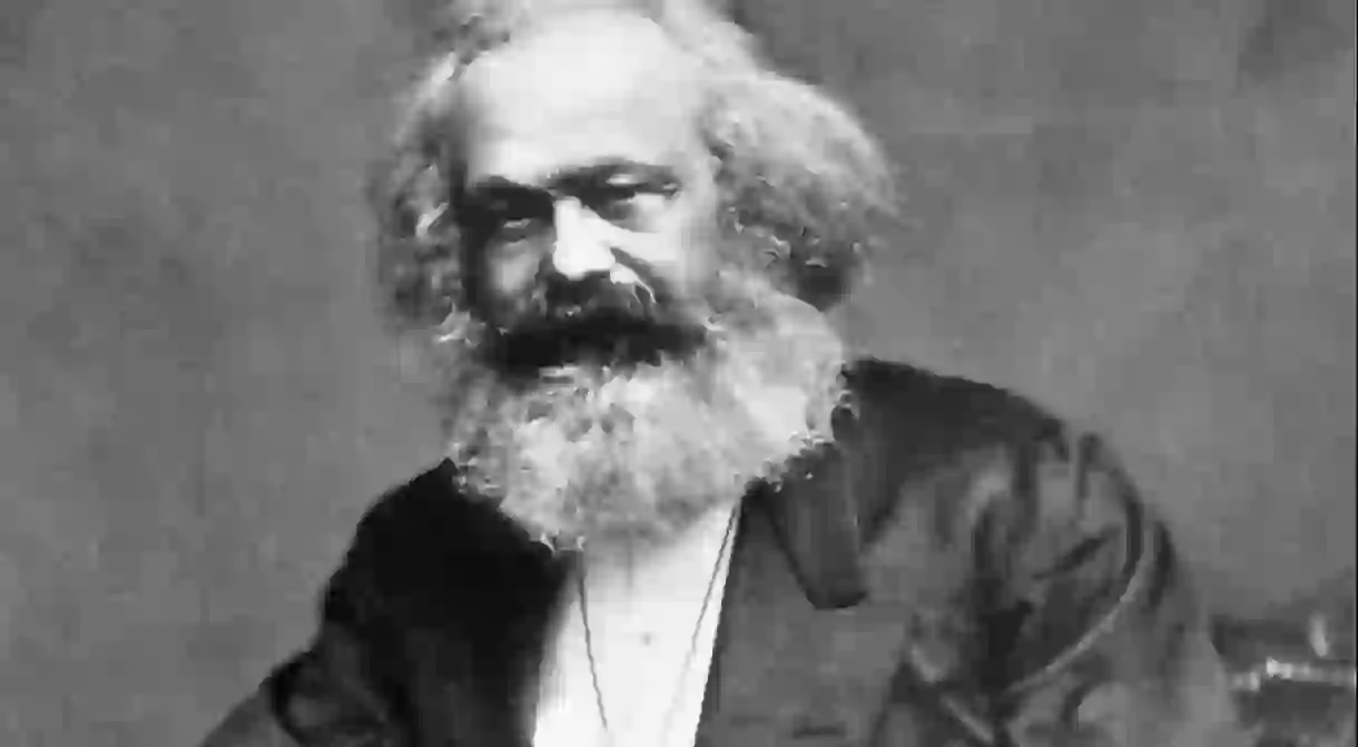 Photographic portrait of Karl Marx seated with a thumb in his lapel and his hand on his thigh, taken in the mid-1870s.