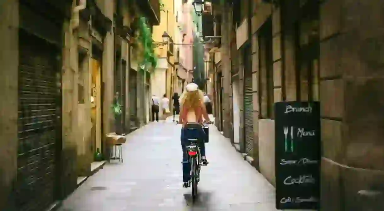 Woman riding bicycle through old street of Barcelona