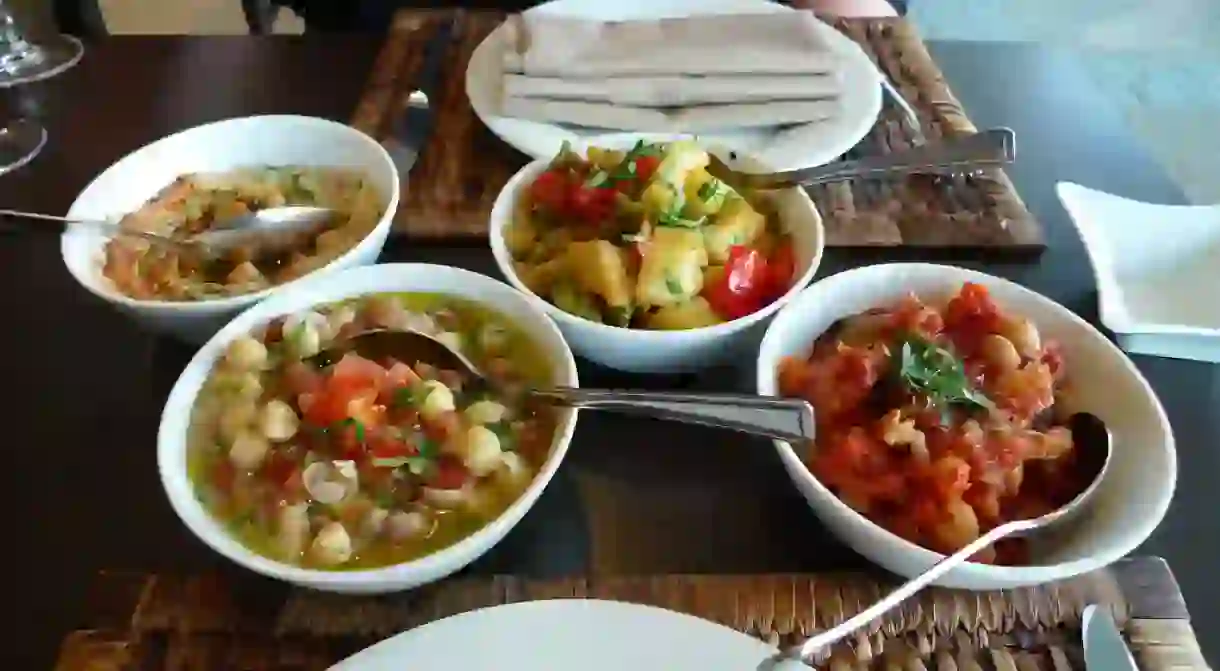 A selection of different Lebanese mezza dishes, L-R: hommos, foul moudamas, batata harra, and moussaka