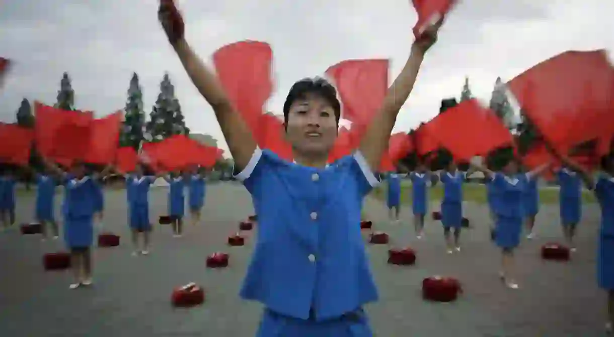 North Korean women wave flags cheering on their fellow countrymen as they start their day during morning rush hour in Pyongyang