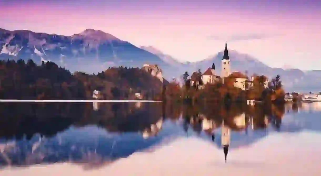 Amazing View On Bled Lake on Sunset. Autumn in Slovenia, Europe. View on Island with Catholic Church in Bled Lake with Castle and Mountains in Background