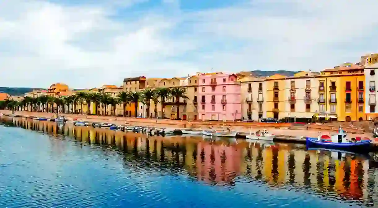 Houses and palm trees along the coast with reflection in bosa, sardegna