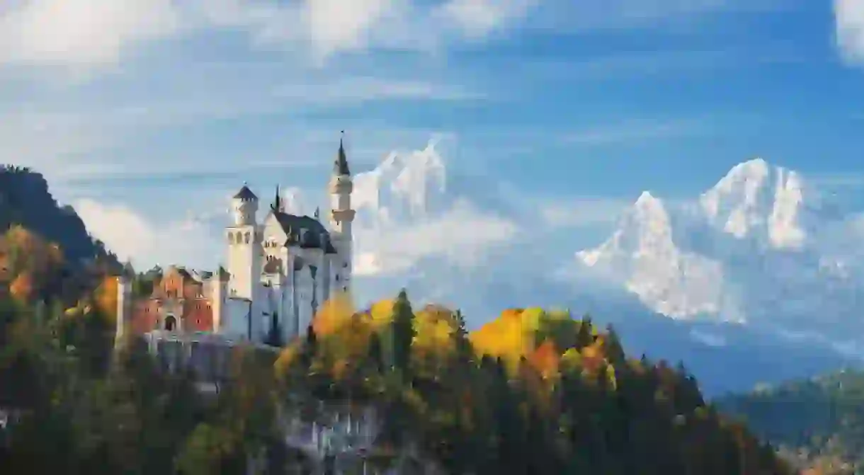 Germany. The famous Neuschwanstein Castle in the background of snowy mountains and trees with yellow and green leaves.