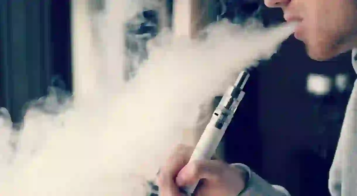 Young man smoking with a vaporizer, which works by heating a liquid to generate an aerosol, commonly called a vapor that the user inhales. From: vaping360.com