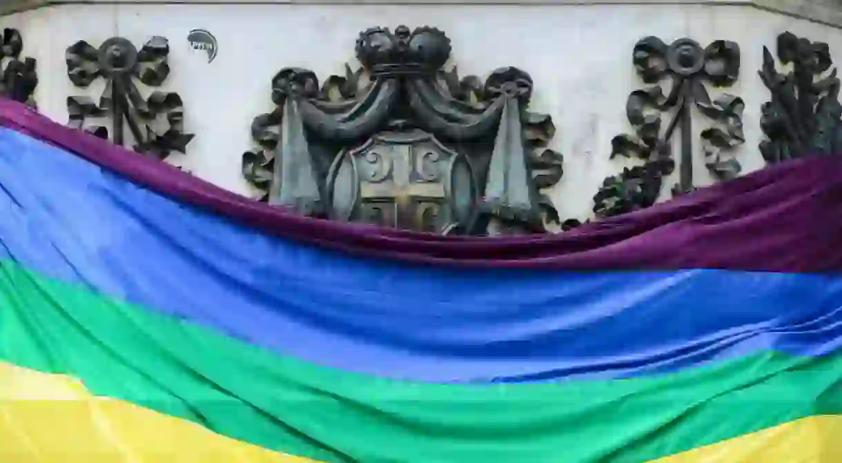 The Pride flag stands in front of the Serbian coat of arms