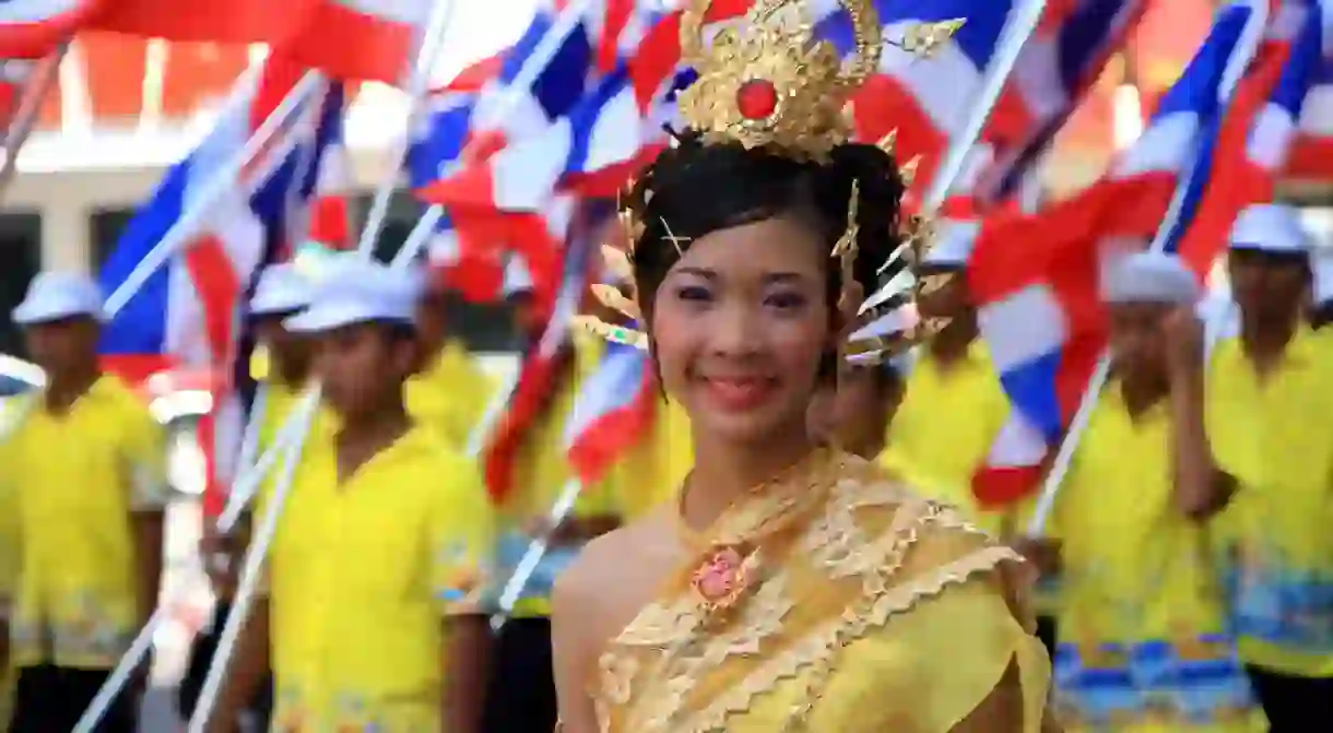 Lady in traditional Thai dress with Thai flags behind her