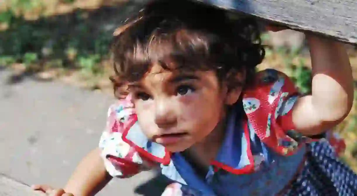 A Roma girl is playing and hiding on a wooden bench, Belgrade, Serbia.