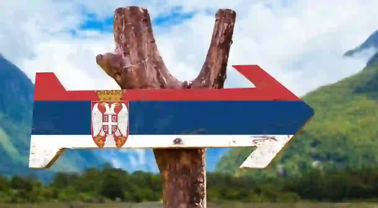 Serbias flag on a wooden sign with mountains in the background