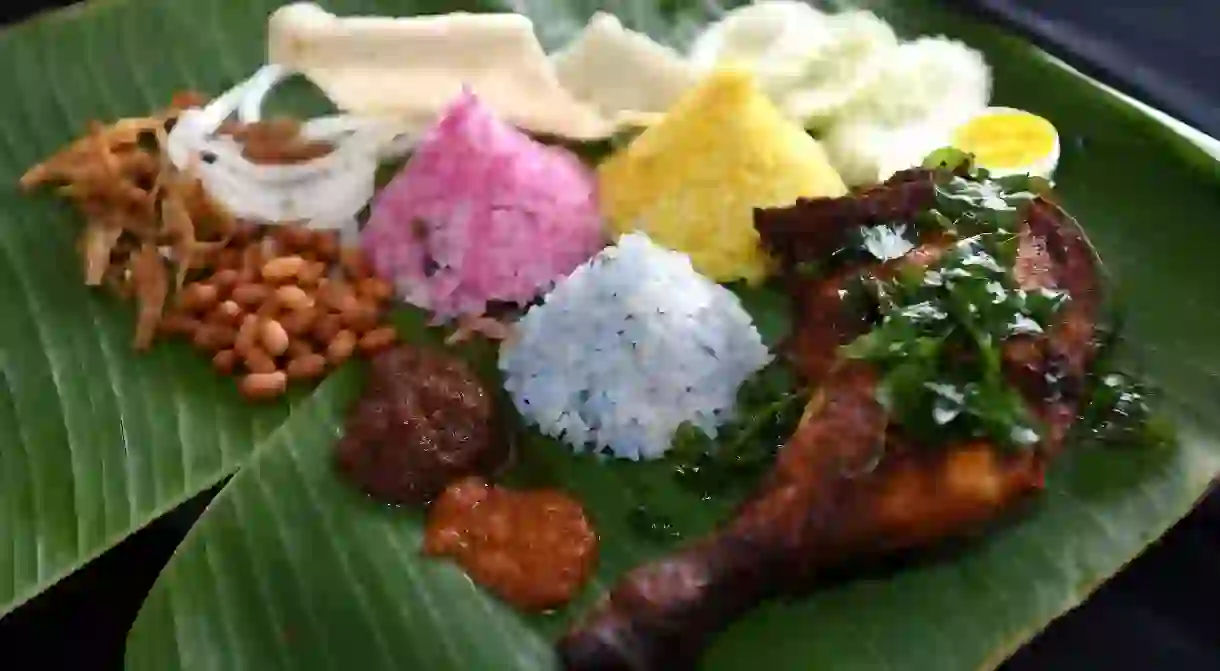 Colorful plate of banana leaf nasi lemak or coconut milk spicy rice with fried chicken drumstick, peanuts and anchovies, prawn crackers, cucumber and egg.