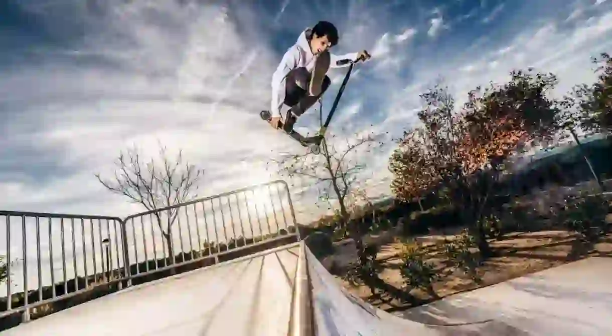 A young man with a scooter makes a jump at a skatepark