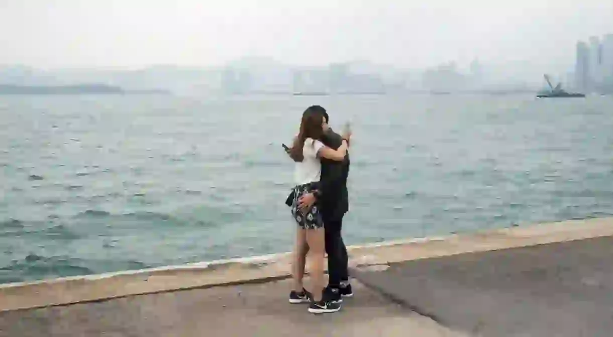 A couple is sharing an embrace while checking their phones at the Instagram Pier, Hong Kong