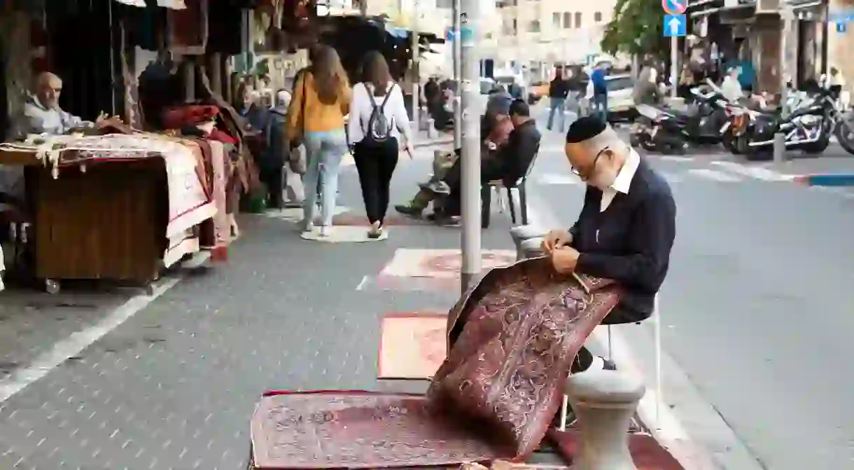 A carpet seller repairing a rug on the street in front of his shop in Old Jaffa, Tel Aviv