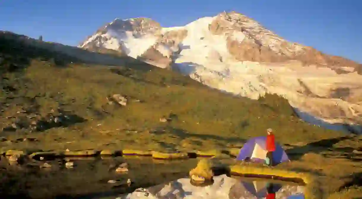 Woman setting up tent by lake below Mount Rainier Mount Rainier National Park, Washington.