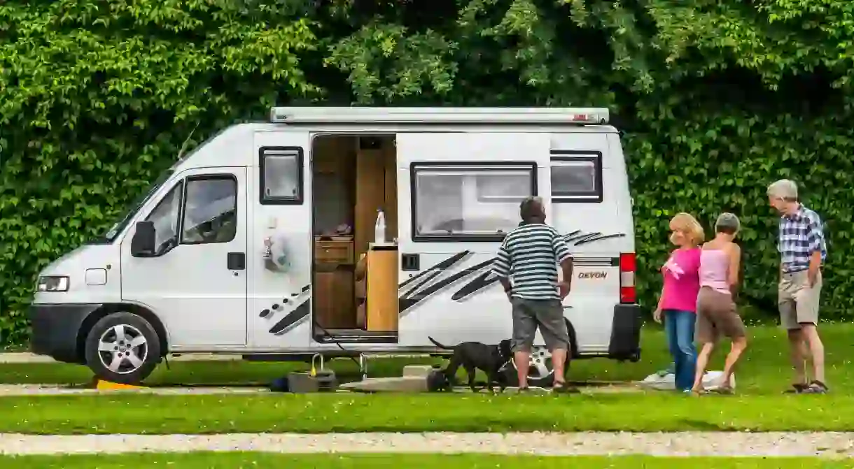 A motorhome couple with their dog, chat to another couple on a Caravan Club campsite pitch in England, UK