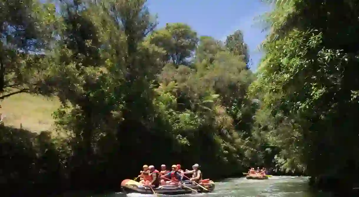 Whitewater rafters paddle over rapids along Kaituna River on summer afternoon