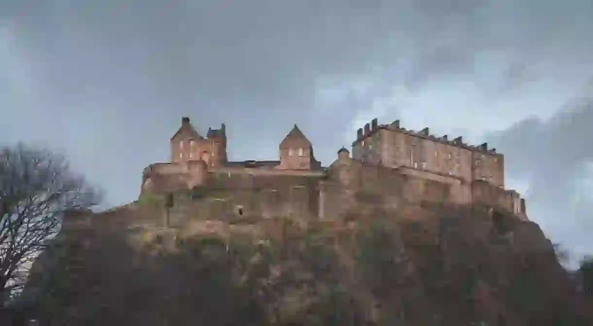 The historic Edinburgh Castle perched atop Castlehill against a moody backdrop on a dark evening in Scotland.