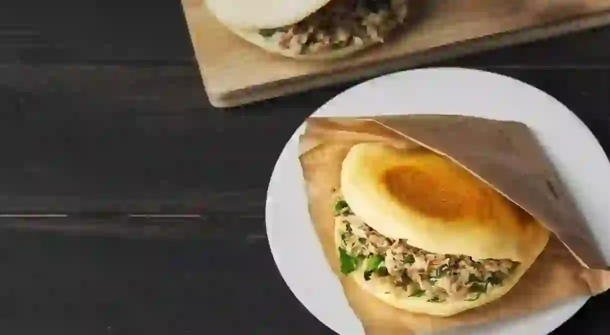 2BXF1ET Rou jia mo Chinese hamburger is a popular street food. Pictured is a homemade sandwich in a white plate on a black wooden table. Top view. Copy space.