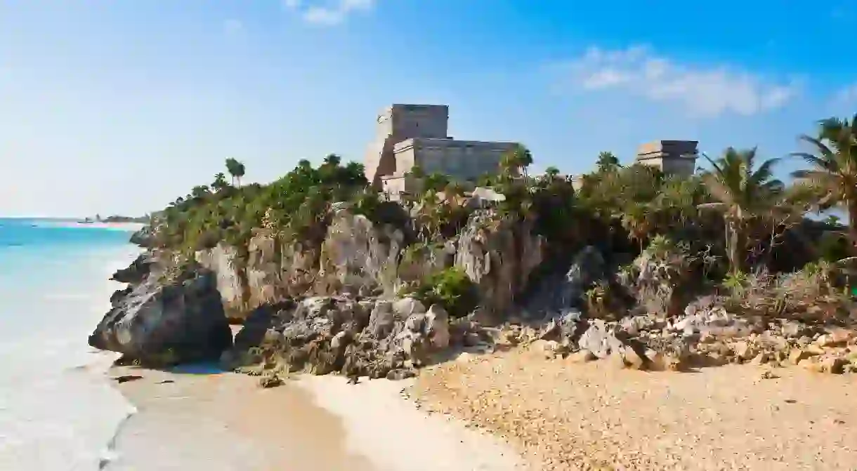 At the Tulum Archaeological Zone, ruins are dotted on the shore alongside palm trees and clear waters