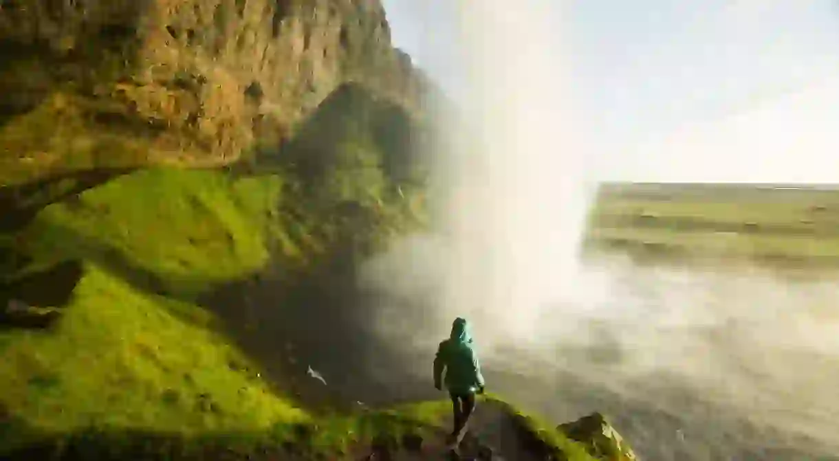 A woman watching the sunset from behind a waterfall in Iceland