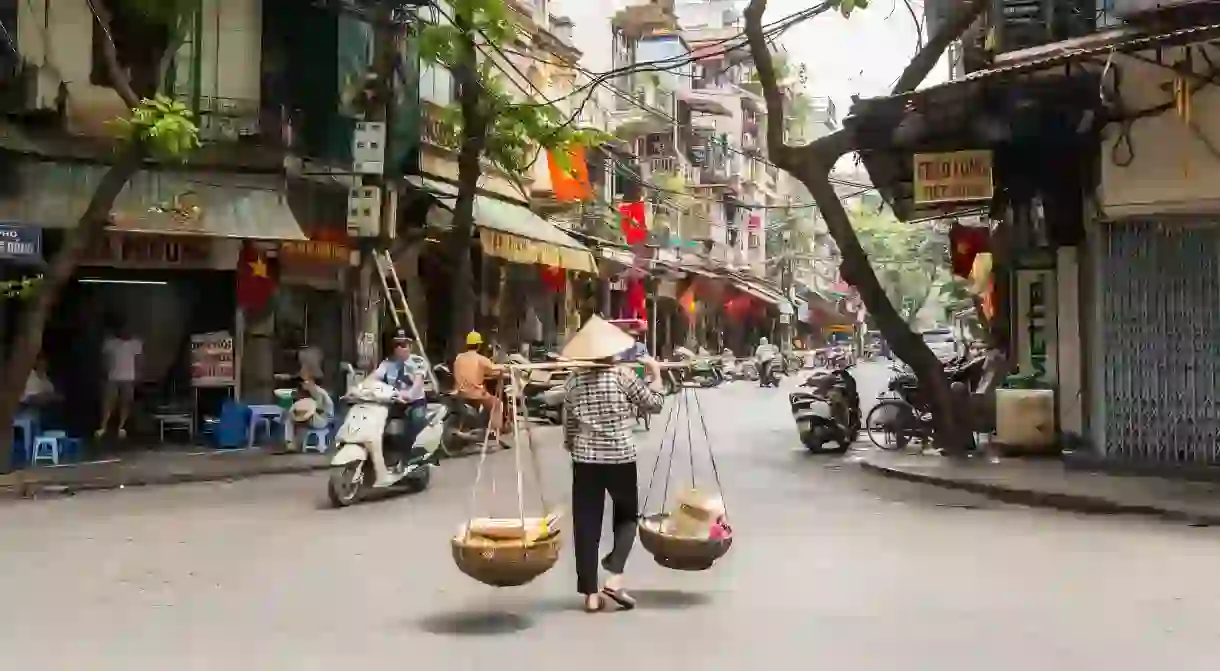 A street vendor transporting goods using baskets and a carrying pole in Hanois Old Quarter