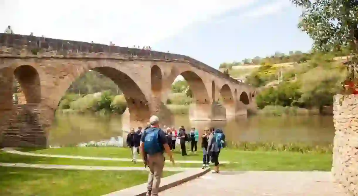 W0YYT4 Pilgrims men woman walking the Camino de Santiago the way of St James by the medieval stone bridge over the river Arga in Puente la Reina Navarra