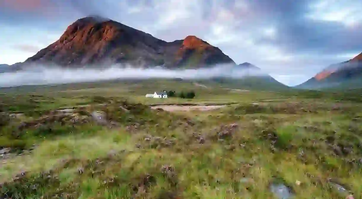 Stunning sunrise over a cottage beneath the mountains at Glencoe in the Scottish Highlands