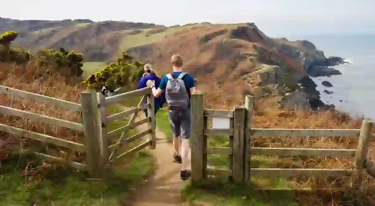 RRNNGD Two people walking on the South West Coast Path and Tarka Trail towards Bull Point from Lee Bay, Ilfracombe, North Devon, England, UK, Britain