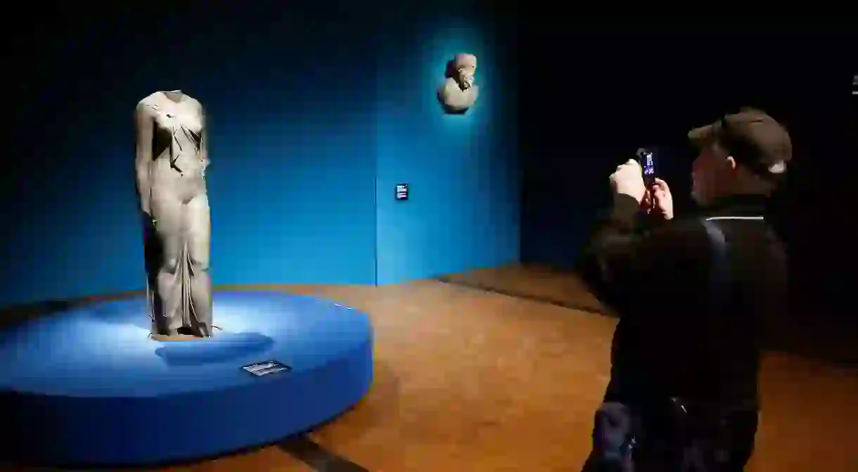 A man takes pictures of a statue during a media preview of the exhibition Osiris - Egypts Sunken Mysteries, which features some 300 objects retrieved from the depths off Egypts Mediterranean coast, at Museum Rietberg in Zurich