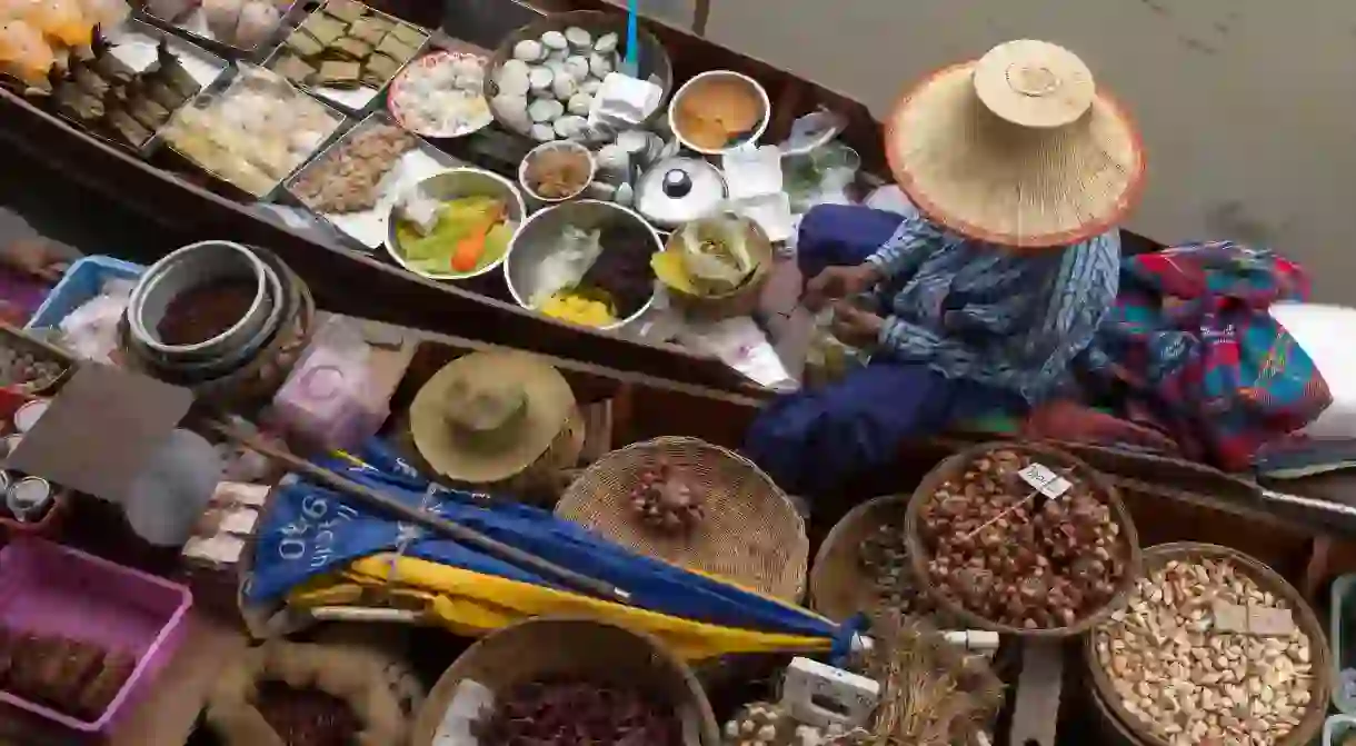 Amphawa Floating Market. Woman prepares food for customer in her dugout canoe shop.