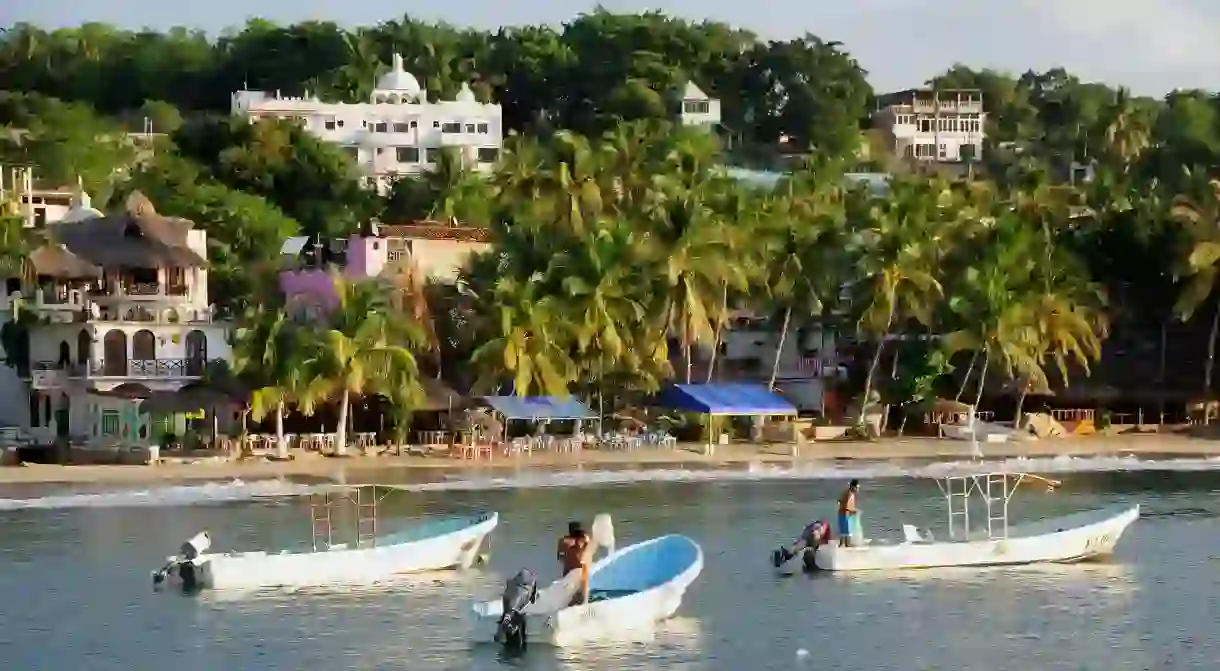 Mexico, Oaxaca, Puerto Escondido, Fishing boats in bay at Playa Marinero beach lined with buildings amongst coconut palm trees.