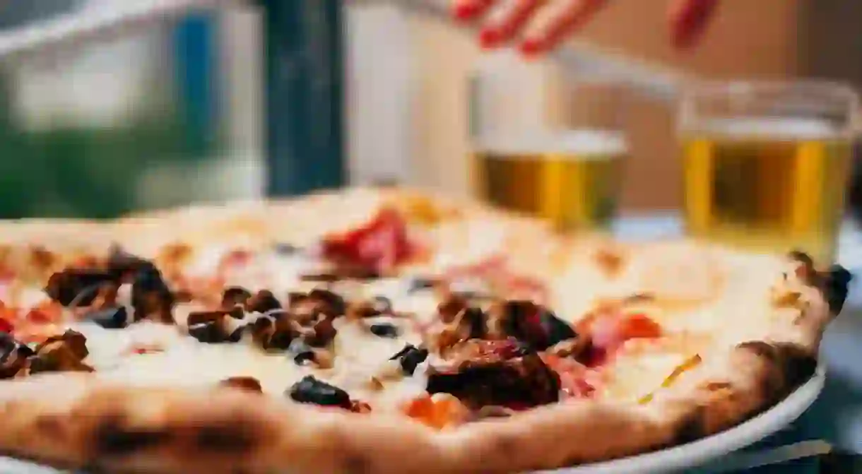 R0NN79 Aubergine pizza on a table and a womans hand reaching for a beer