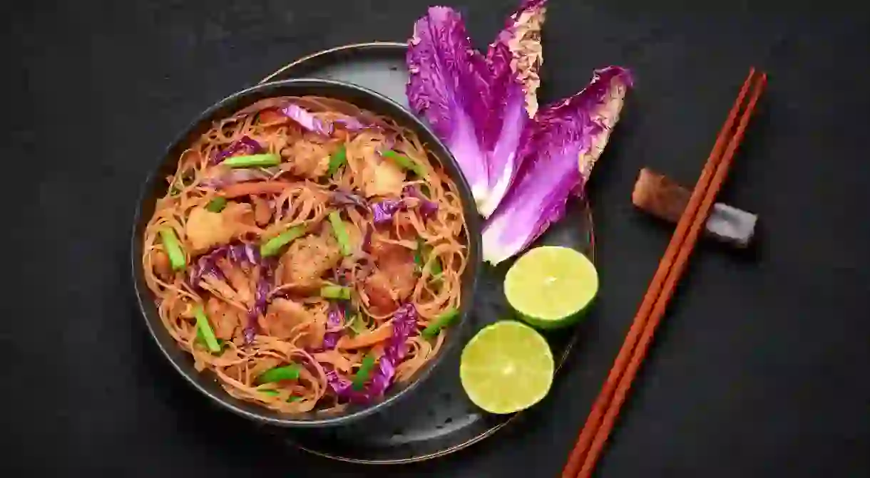 2EAY5PT Pancit Bihon in black bowl on dark slate table top. Filipino cuisine noodles dish with pork belly, chicken, vegetables. Asian food. Top view