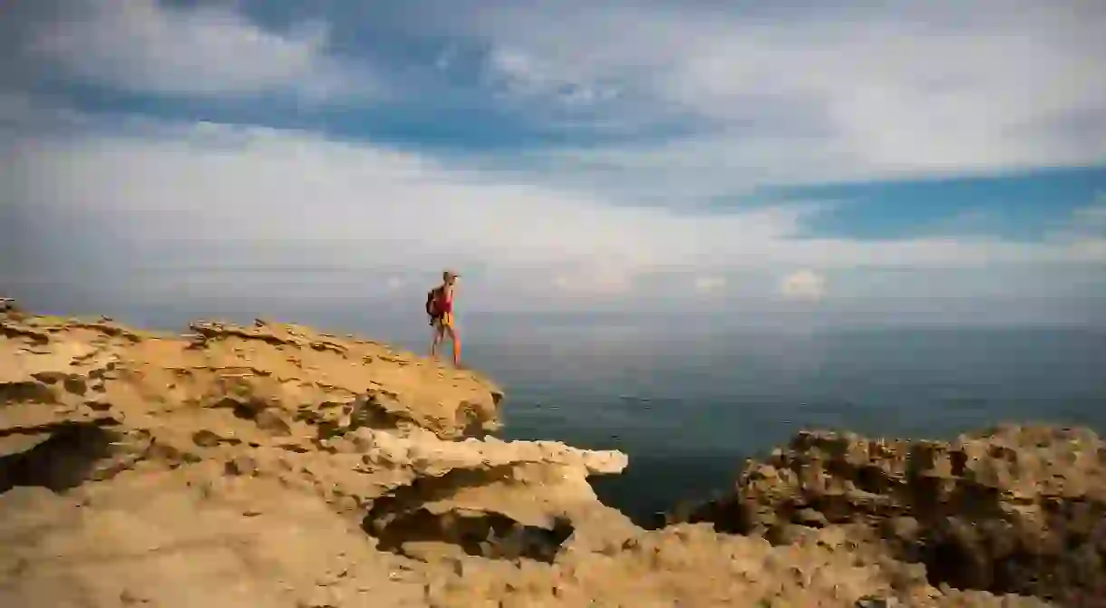 A hiker standing on top of rocks looking out at a blue sea