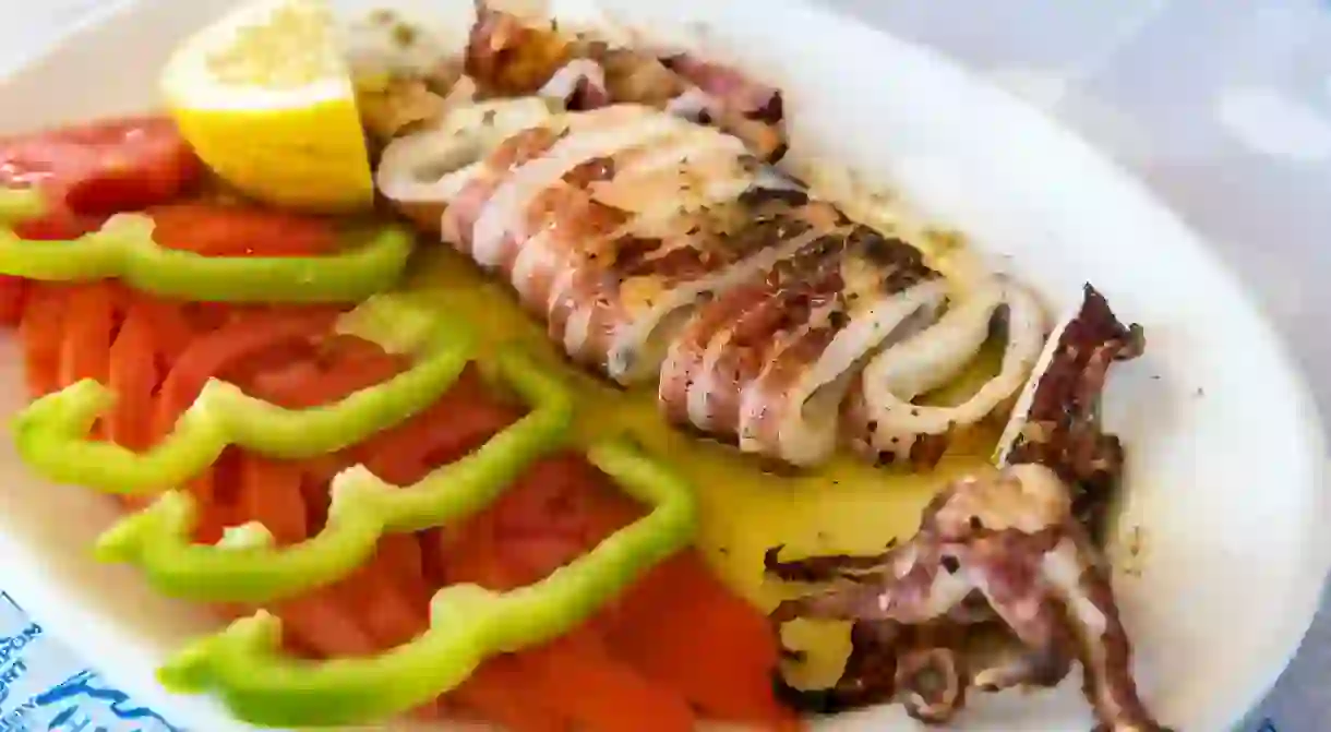 KYYT7N Seafood, grilled calamari served with tomatoes, green peppers and lemon in traditional Greek tavern. Naxos island. Greece.