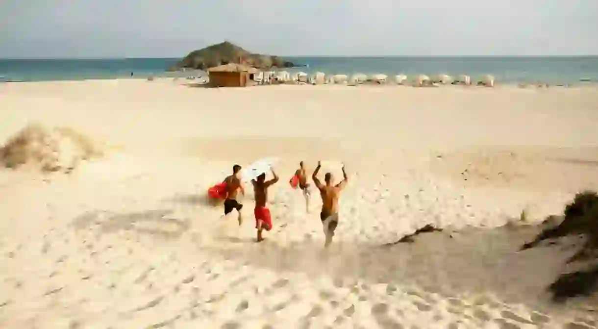 Young surfers running toward the water with surfing board from sand dunes