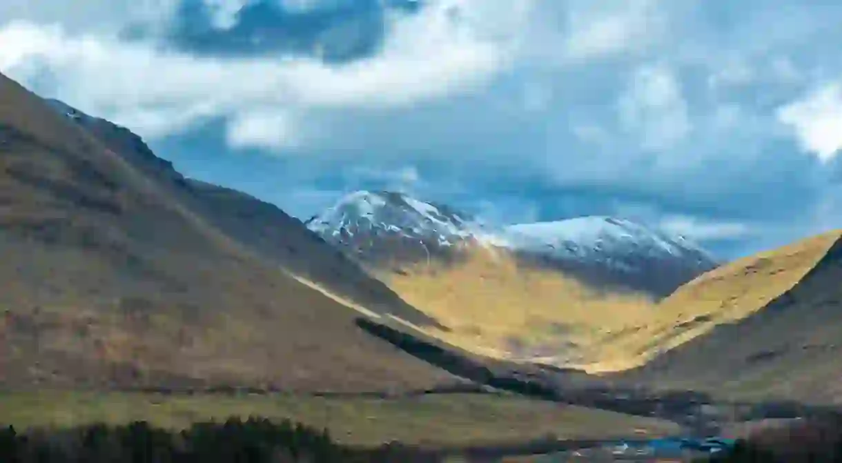 A valley in the Scottish Highlands,nestled between mountains with trees.