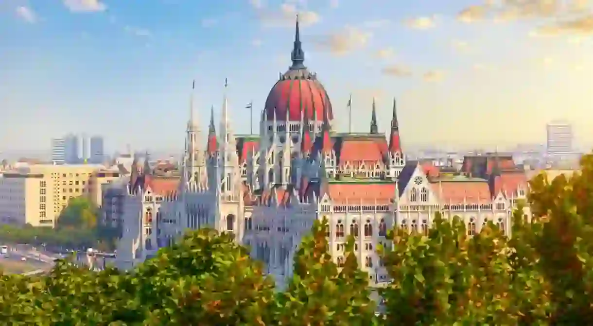 Panorama with Budapest Hungarian Parliament building at Danube river in city, Hungary. Scenic summer panoramic view. Green trees and blue dramatic sky clouds.