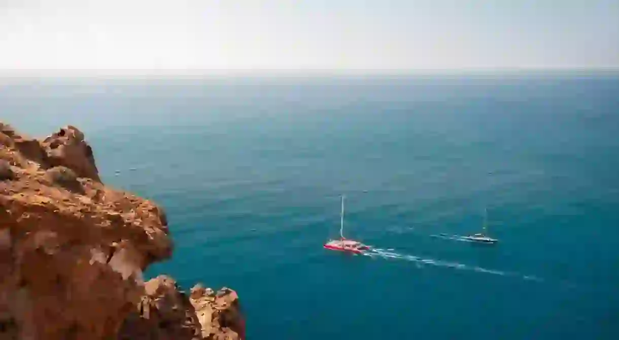 Santorini island, Greece. Yachts sailing near the sea coast. Clear blue sea and red volcanic rocks. Summer seascape.