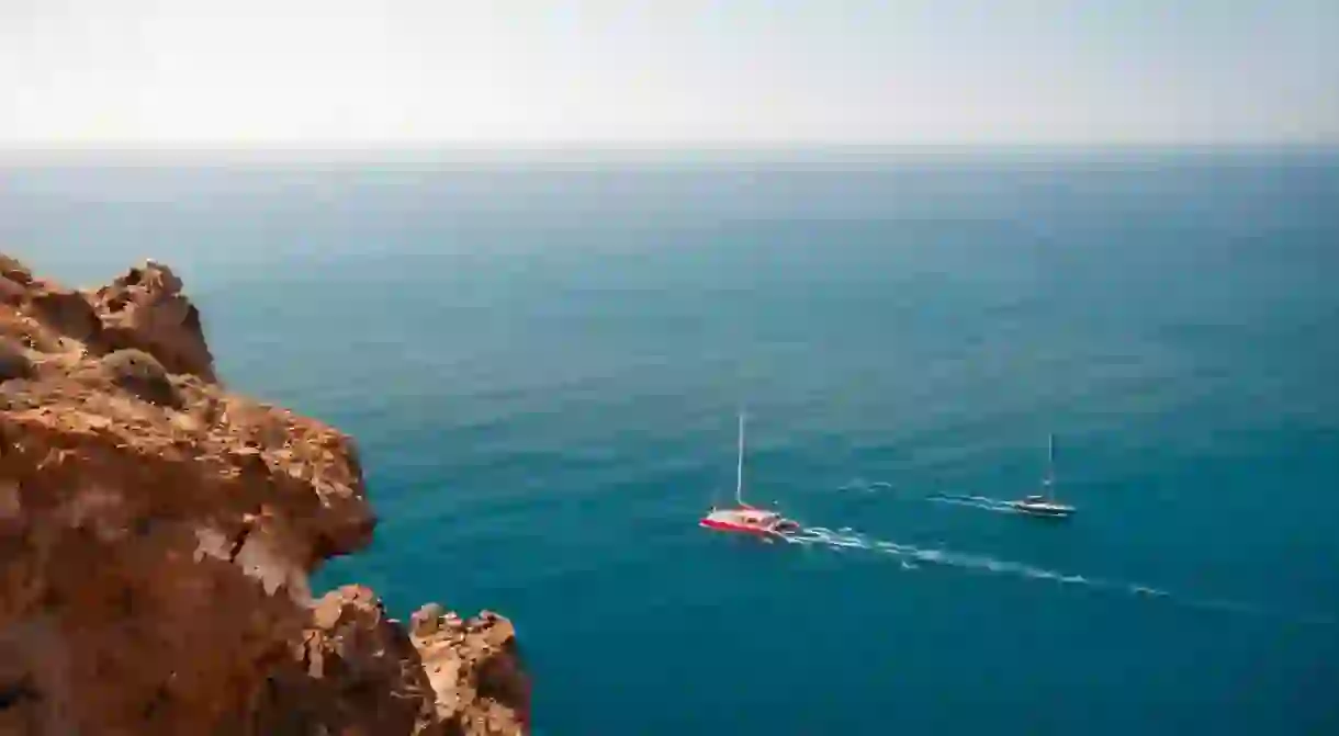 Santorini island, Greece. Yachts sailing near the sea coast. Clear blue sea and red volcanic rocks. Summer seascape.