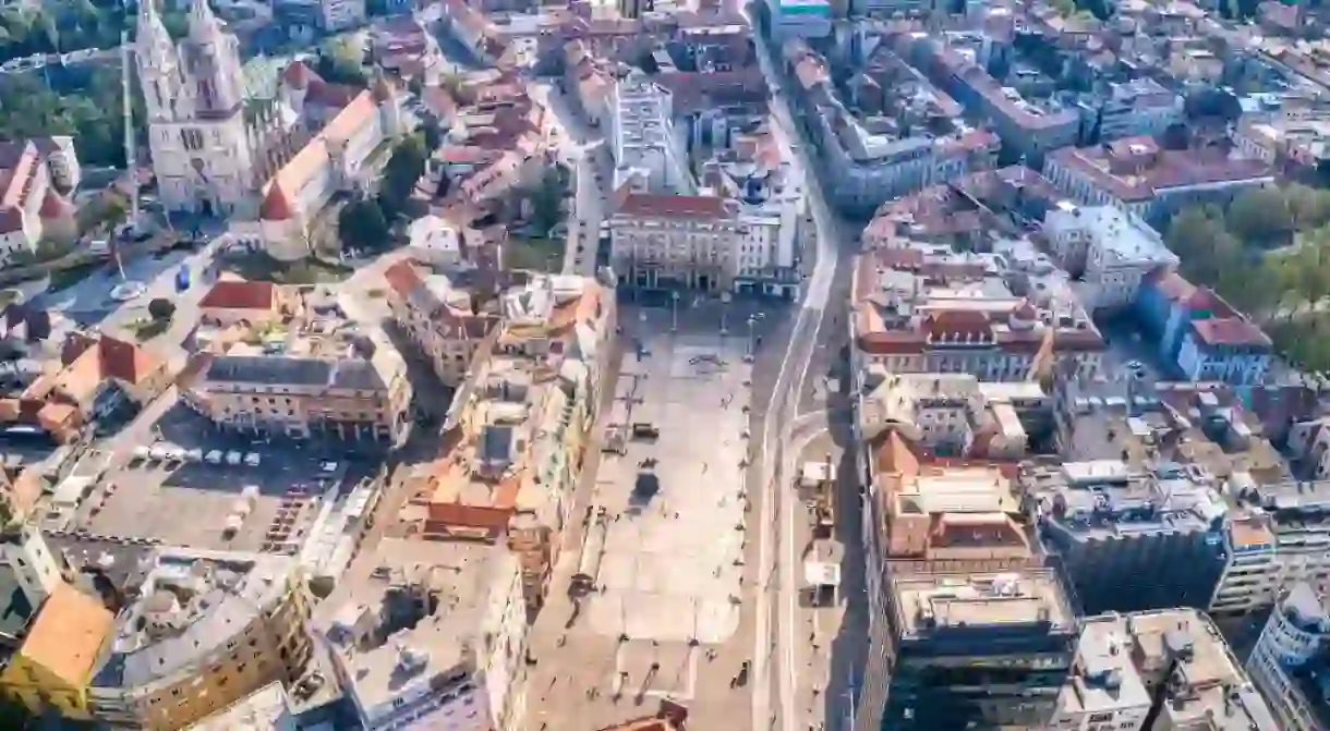 Aerial view of the bustling Josipa Bana Jelačića Square in Zagreb, Croatia, showcasing historic buildings, the iconic cathedral, and city streets.