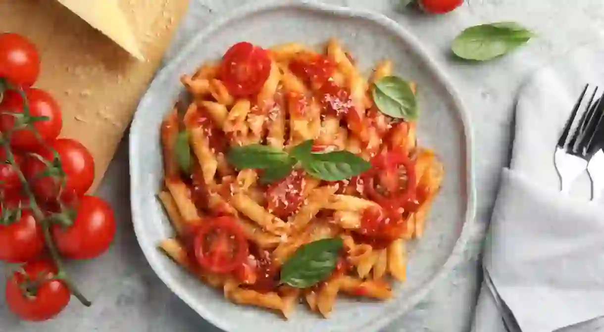 Delicious pasta with tomato sauce, basil and cheese on served gray textured table, flat lay