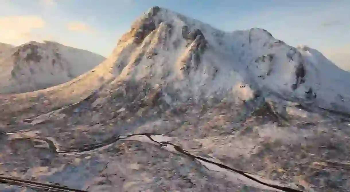 Golden light illuminating iconic snowcapped Scottish mountain range Buachaille Etive Mor.