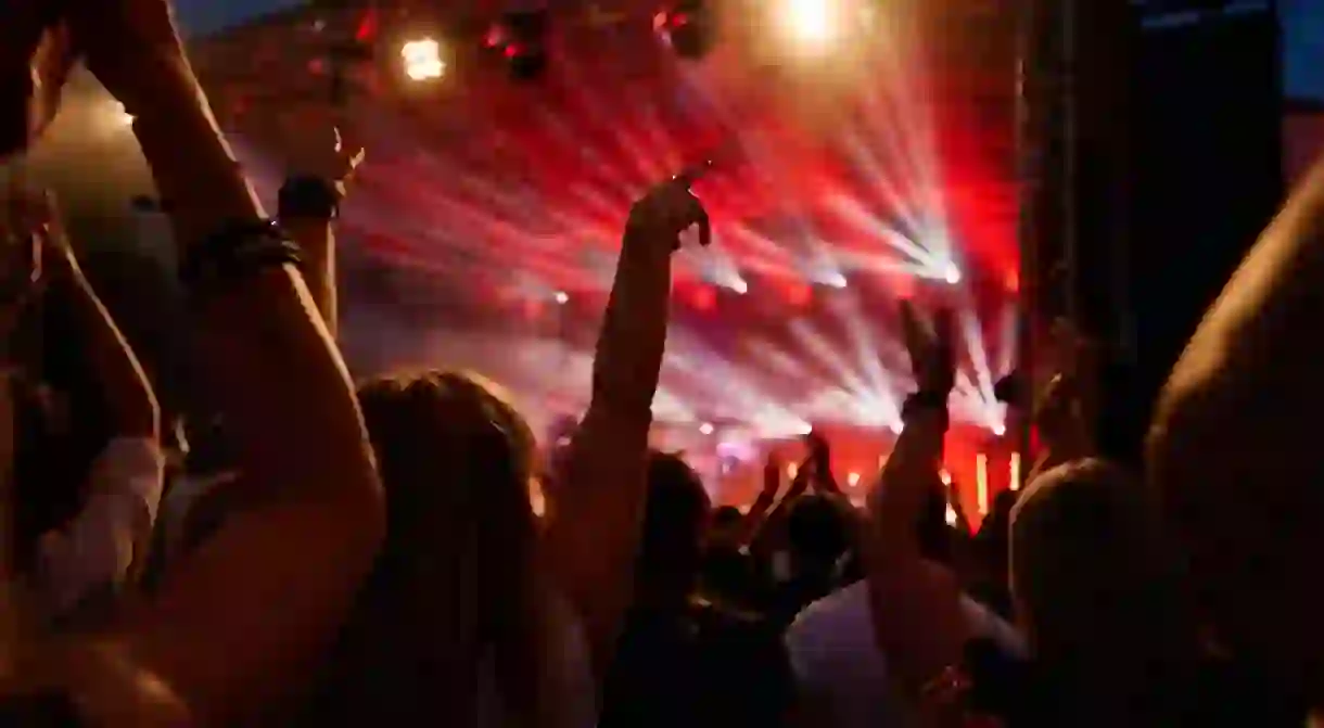 Silhouettes of crowd at concert in front of stage with bright spotlights.