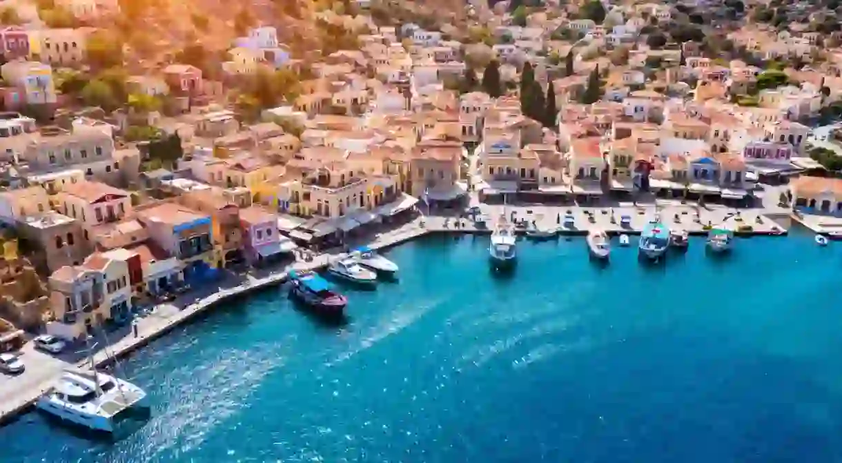 View on Symi (Simi) island harbor port, classical ship yachts, houses on island hills, Aegean Sea bay.