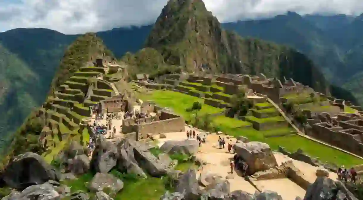 Machu Picchu ruins with tourists with dramatic clouds, Machu Picchu historical Sanctuary, Cusco, Peru.