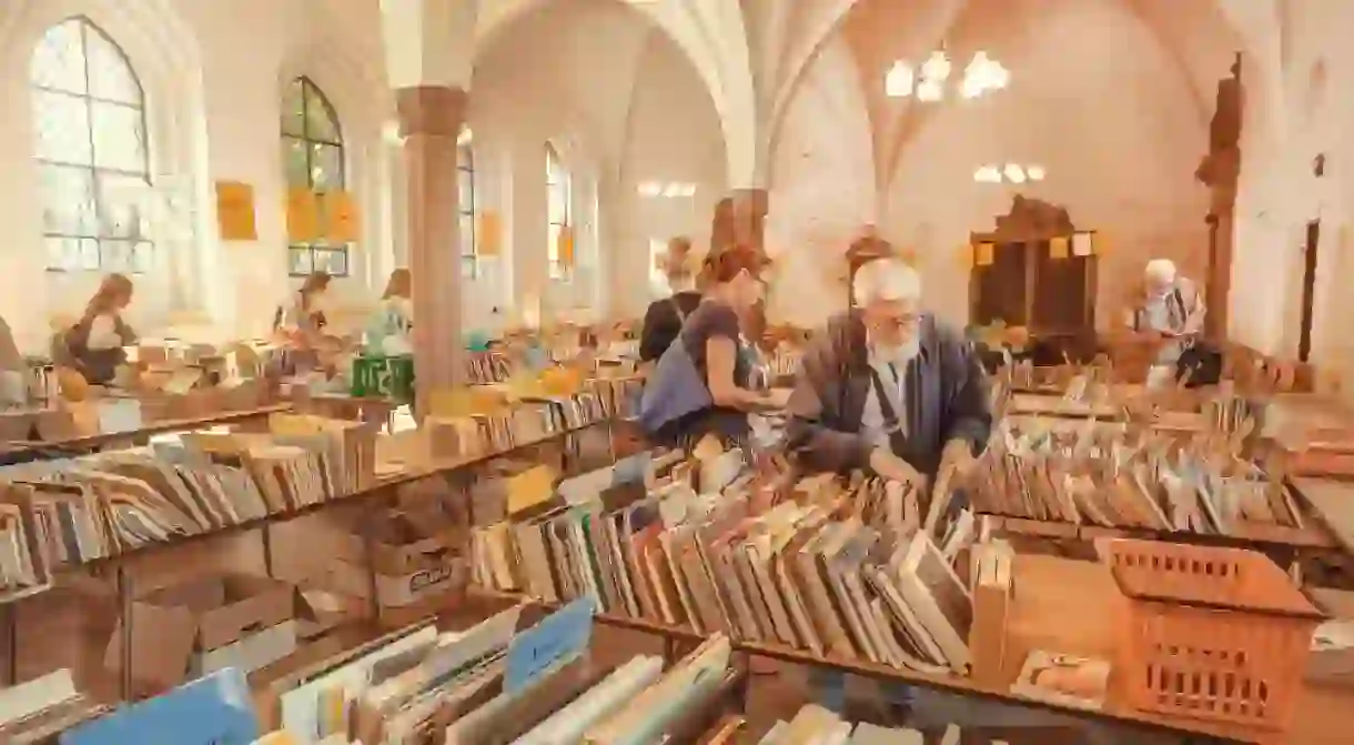 Man and other readers making choice and buying books at flea market in historical church, Copenhagen