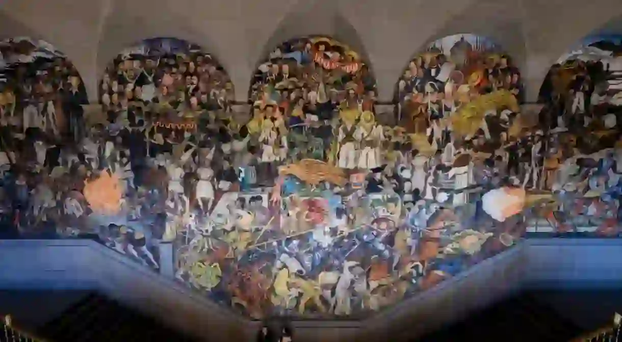 A couple looks at the History of Mexico mural by Diego Rivera at Palacio Nacional (National Palace) in Mexico City